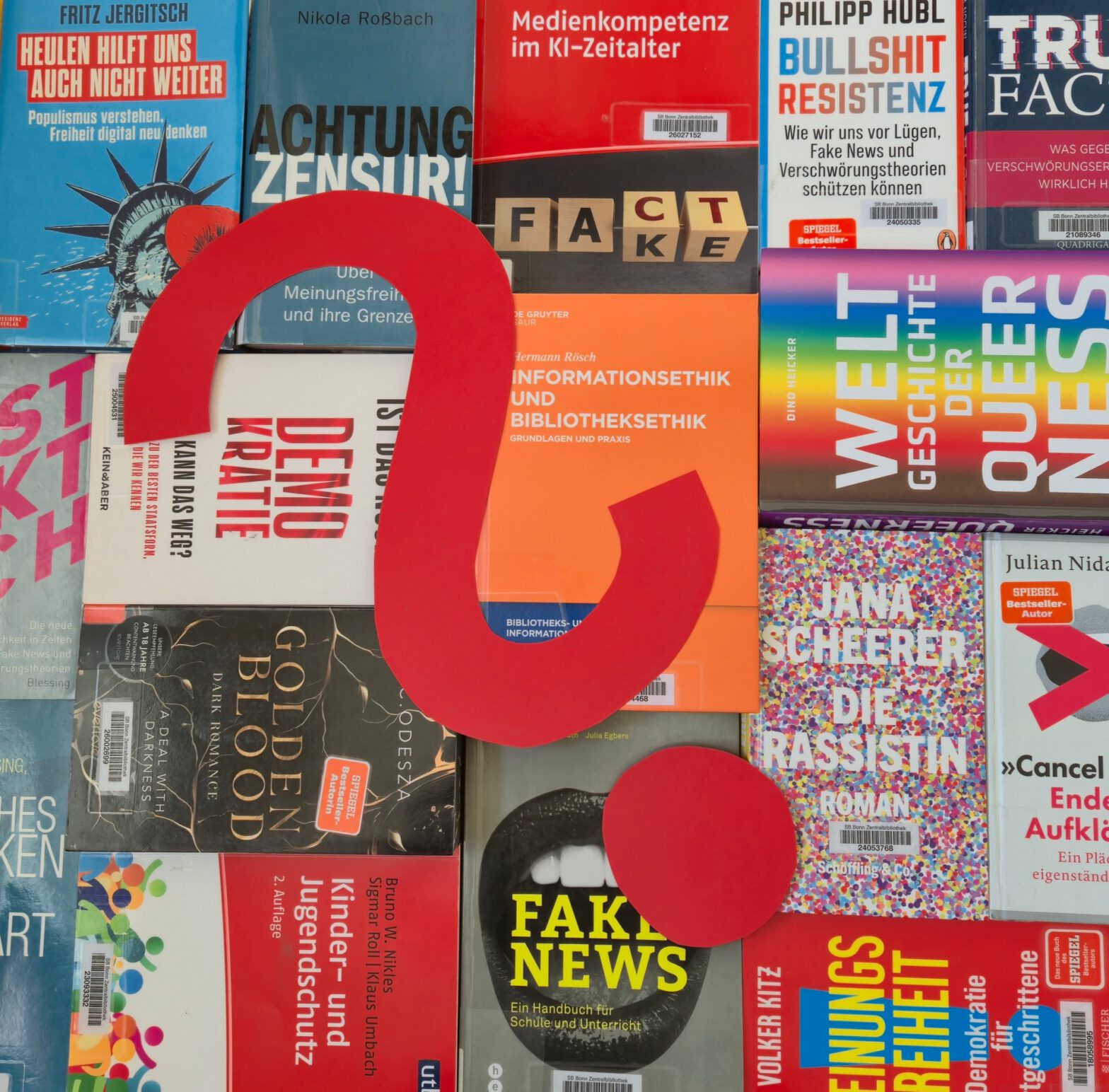 Foto zur Veranstaltung "Bücher verbieten?" mit vielen Büchern, die auf einem Tisch liegen, deren Cover man von oben sieht. Auf den Büchern liegt ein großes rotes Fragezeichen.